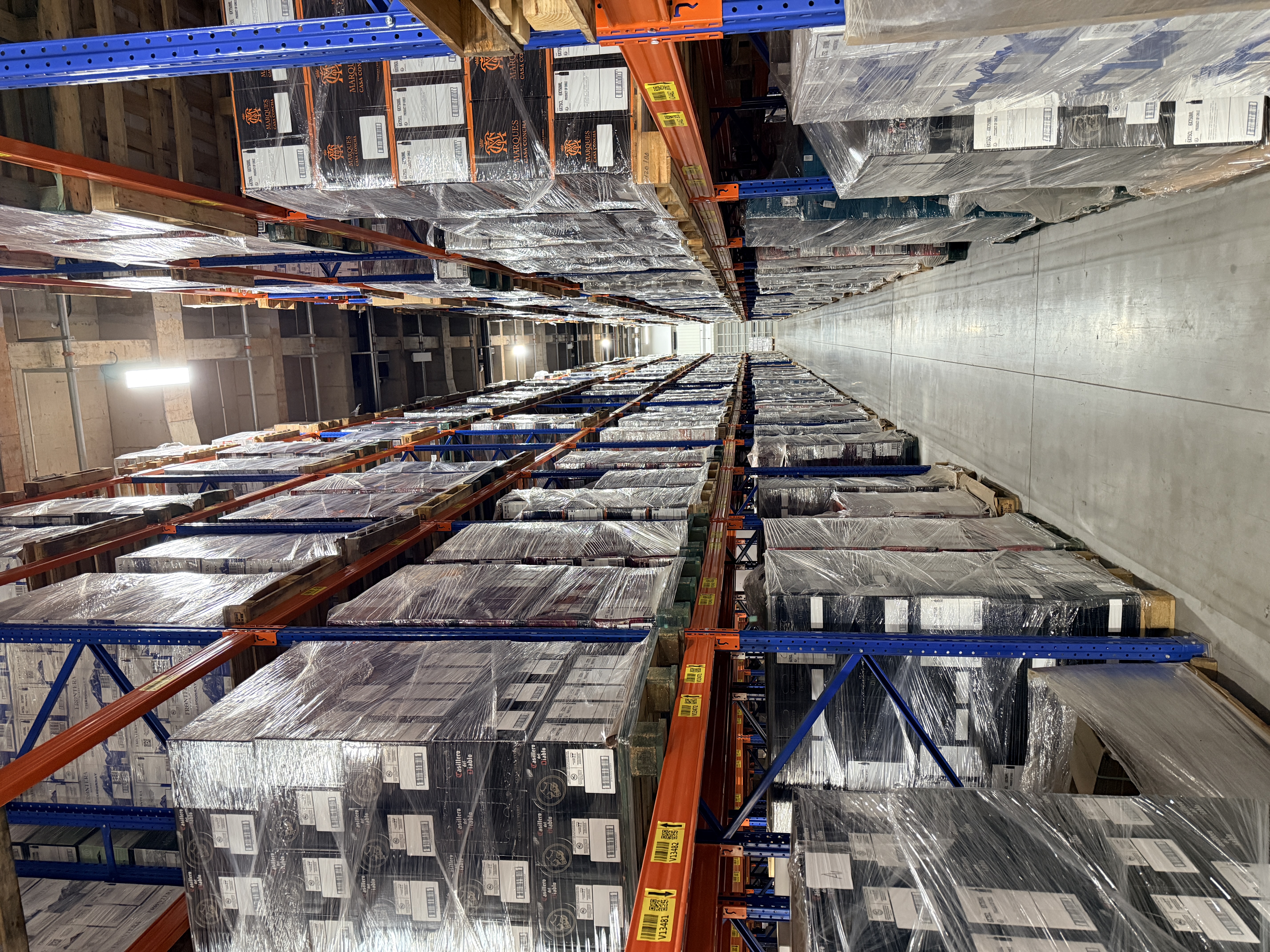 Palletised wine on both sides of the aisle, with location labels on the rack beams.