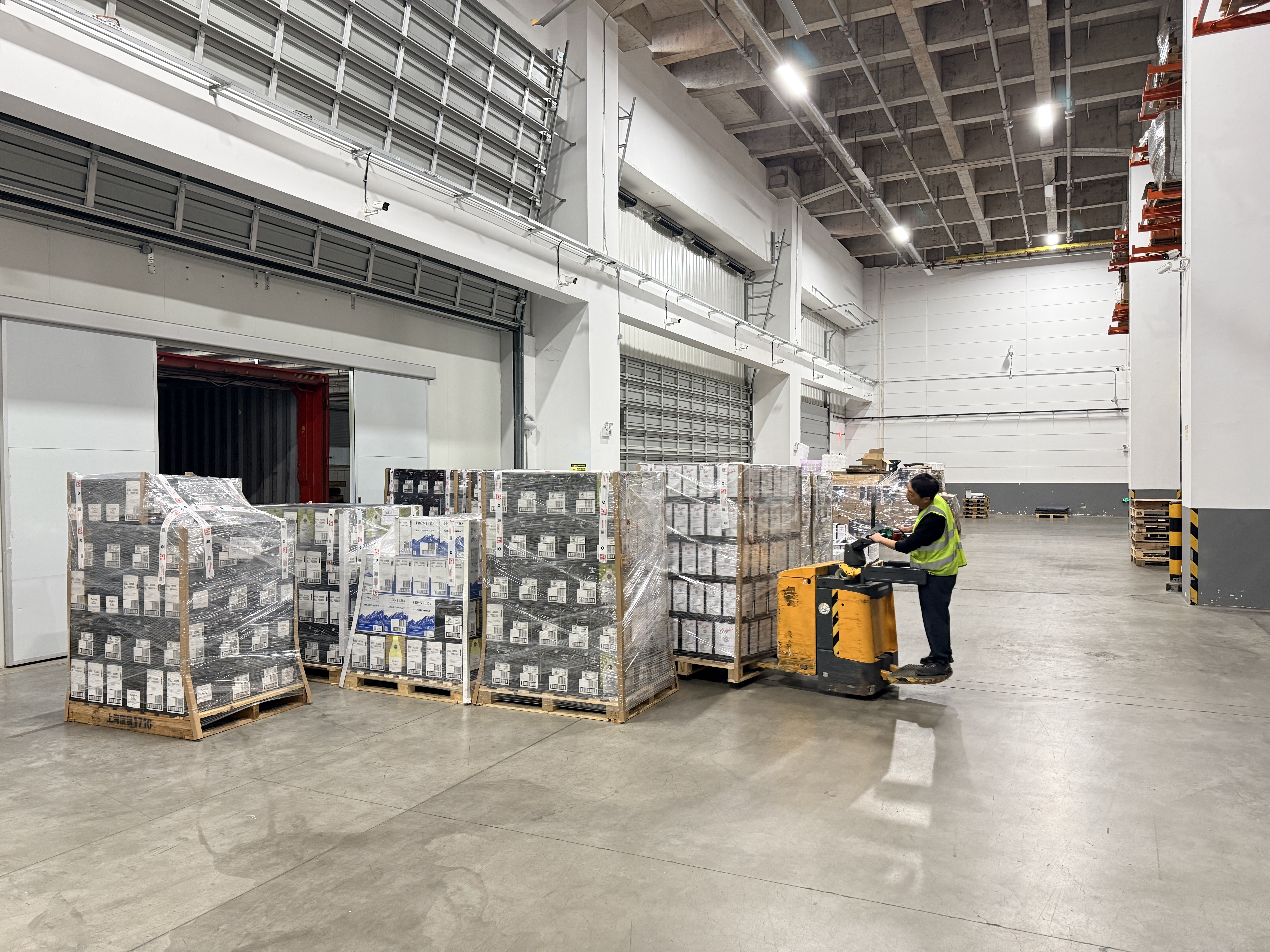 An operator moves palletised wine with an electric pallet truck inside the loading bay.